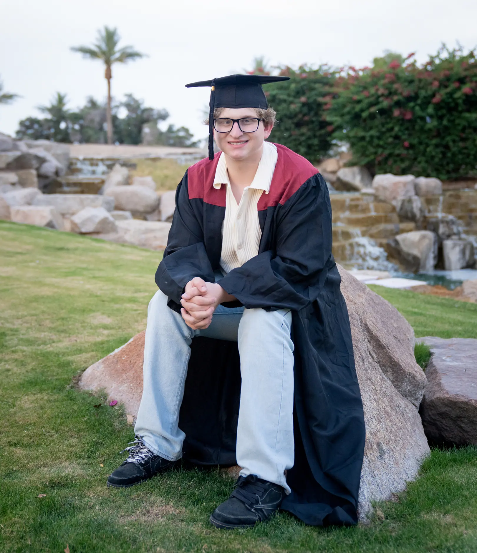 Jackson in his graduation cap and gown seated on a rock outdoors